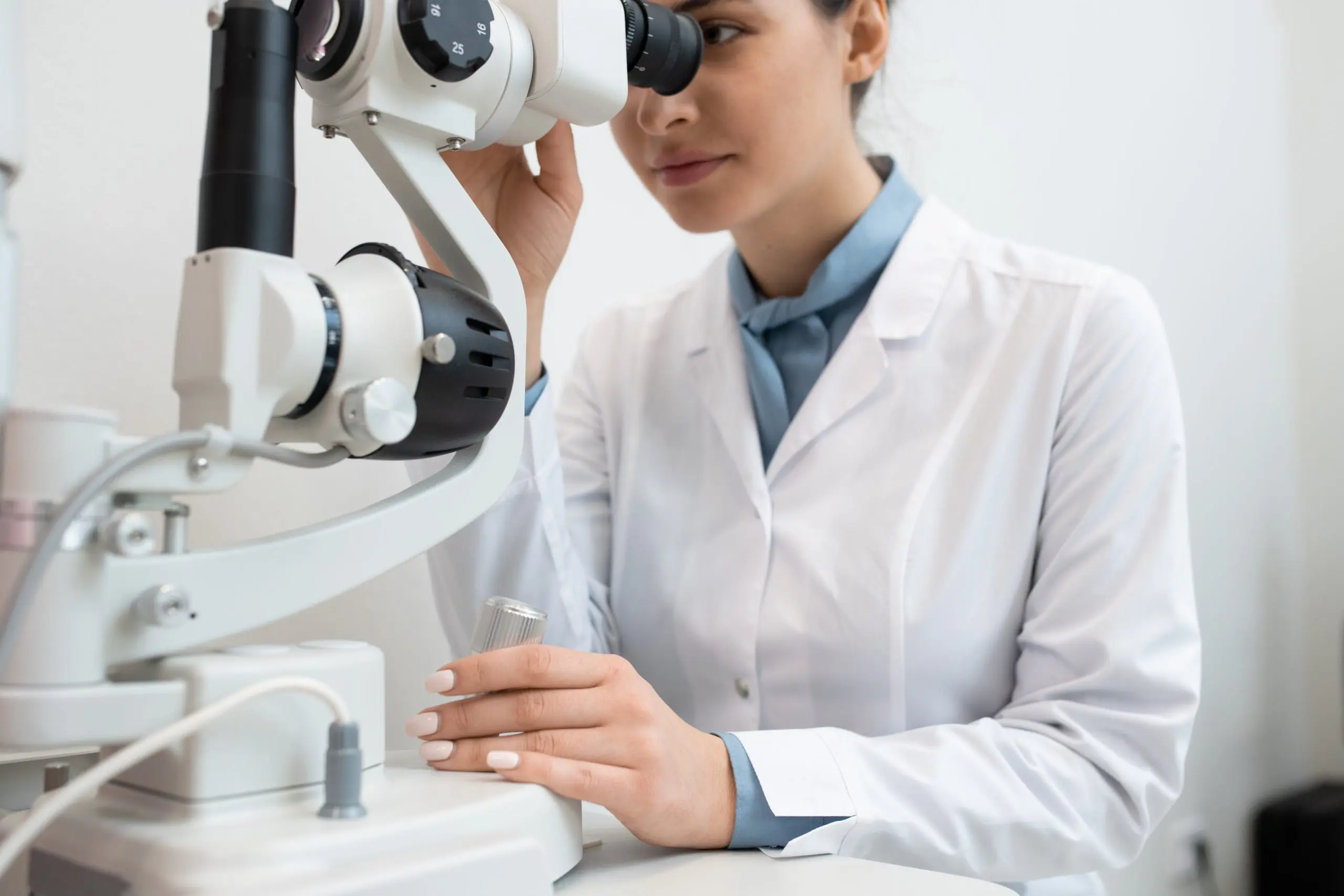 Young female ophthalmologist in whitecoat using new medical equipment to check up eyesight of one of clients in contemporary clinics