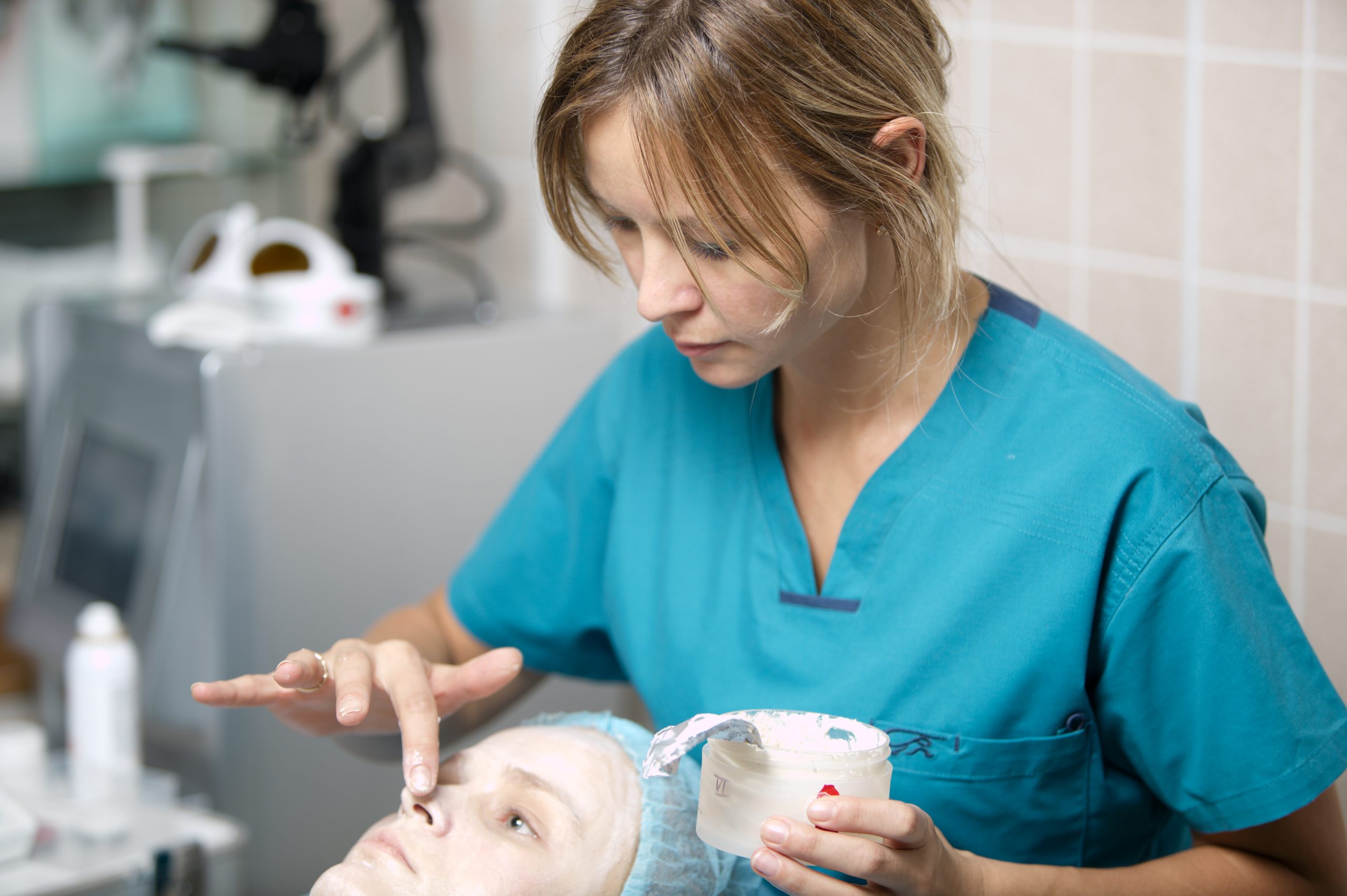 Nurse in a skincare clinic applying protective cream to the delicate skin around the nostrils and eyes of a female patient lying on the surgical couch